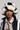 A person wearing a black and white BROOKFIELD FAUX FUR BUCKET HAT, a snake-patterned shirt, and a matching black and white jacket stands out against the neutral background, highlighting this chic winter accessory.