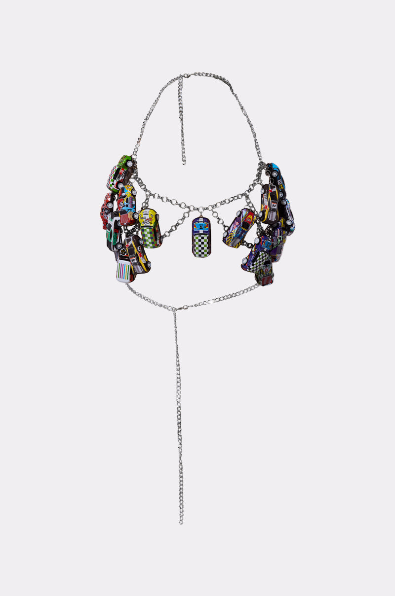 The I GO FAST RACE CAR BODY CHAIN features a silver metallic chain with colorful, geometric enamel charms and pendants in clusters. A single long chain hangs from the center, all set against a plain white background.