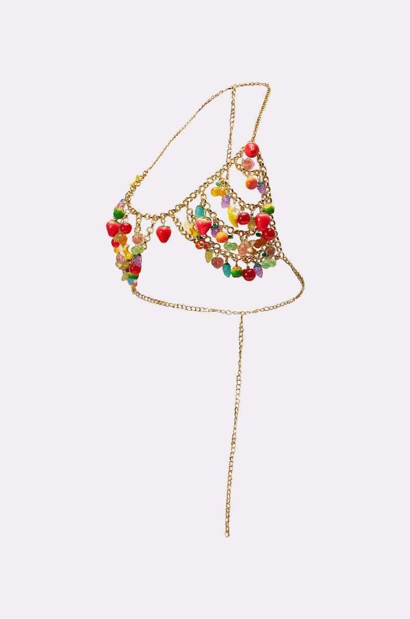 The TASTE ME FRUITY BODY CHAIN is a gold bralette adorned with colorful beads, charms, and red heart accents. Displayed on a plain background, it features a long dangling chain—an ideal playful accessory for festivals. 9