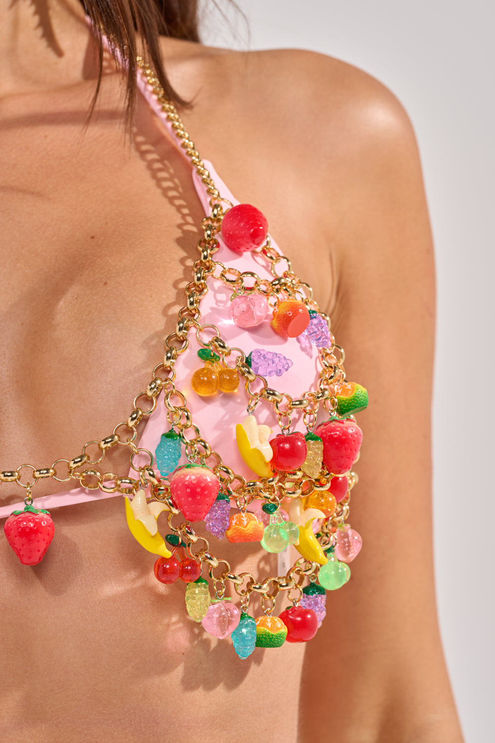 A close-up of a woman wearing a pink bikini top and the TASTE ME FRUITY BODY CHAIN, adorned with colorful fruit charms—strawberries, cherries, bananas, grapes—for the perfect festival accessory. 6