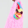 The person is dressed in a long, fluffy pink coat adorned with colorful knitted details on the shoulder and sleeve. They are carrying the "I LOVE YOU Faux Fur Oversized Tote" in bubblegum pink, adding a playful touch. The background is plain and light-colored.