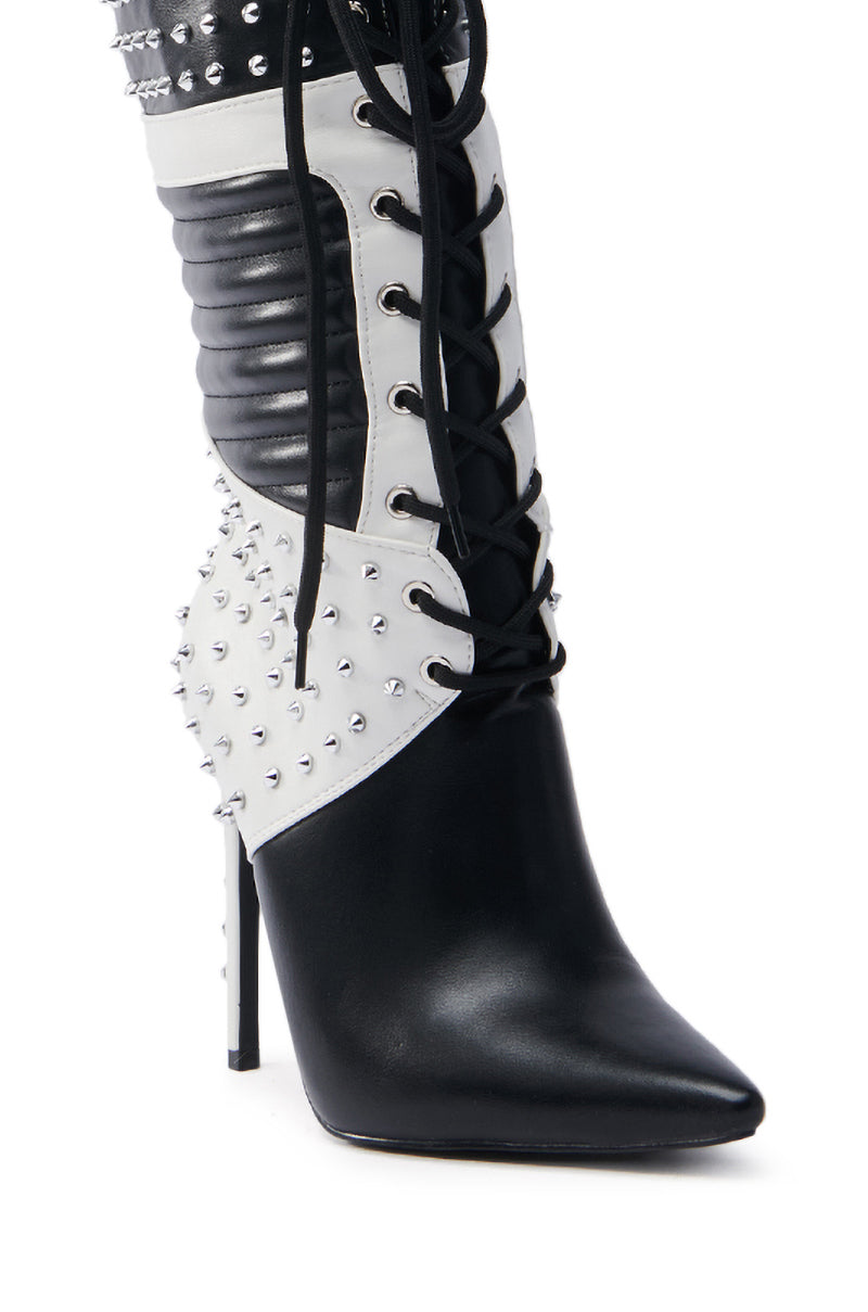 The AZALEA WANG OCTOBI BLACK AND WHITE STILETTO BOOT is a high-heeled boot with a pointed toe, showcasing a bold design. It features a faux leather upper, lace-up front, quilted detailing, and silver studs for an edgy appearance.