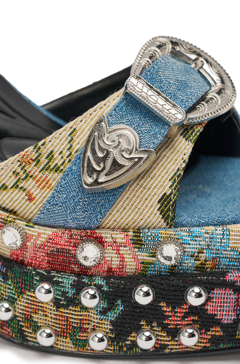 A close-up of the AKIRA GOLD ODE DENIM MULTI CHUNKY RHINESTONE SANDAL, featuring denim and brocade floral tapestry straps, silver Western-style buckles, a studded platform chunky heel, and colorful floral detailing. 6