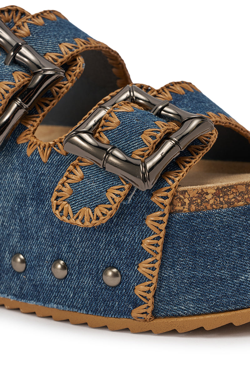 Close-up of the AZALEA WANG OHKAY DENIM FLAT PLATFORM SANDAL featuring denim straps with tan zigzag stitching, two oversized silver buckles, a brown cork-style footbed, black rivets, and a textured tan sole—ideal for summer style. 6