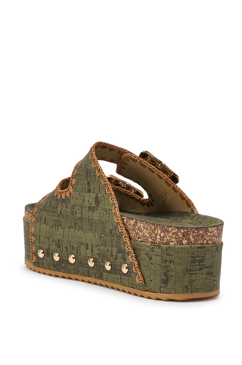 The AZALEA WANG OHKAY GREEN FLATFORM STUD EMBELLISHED SLIP ON SANDAL features olive green crisscross straps, a cork flatform sole, tan stitching, metallic studs on the sides, and a thick patterned sole for an earthy look. 5