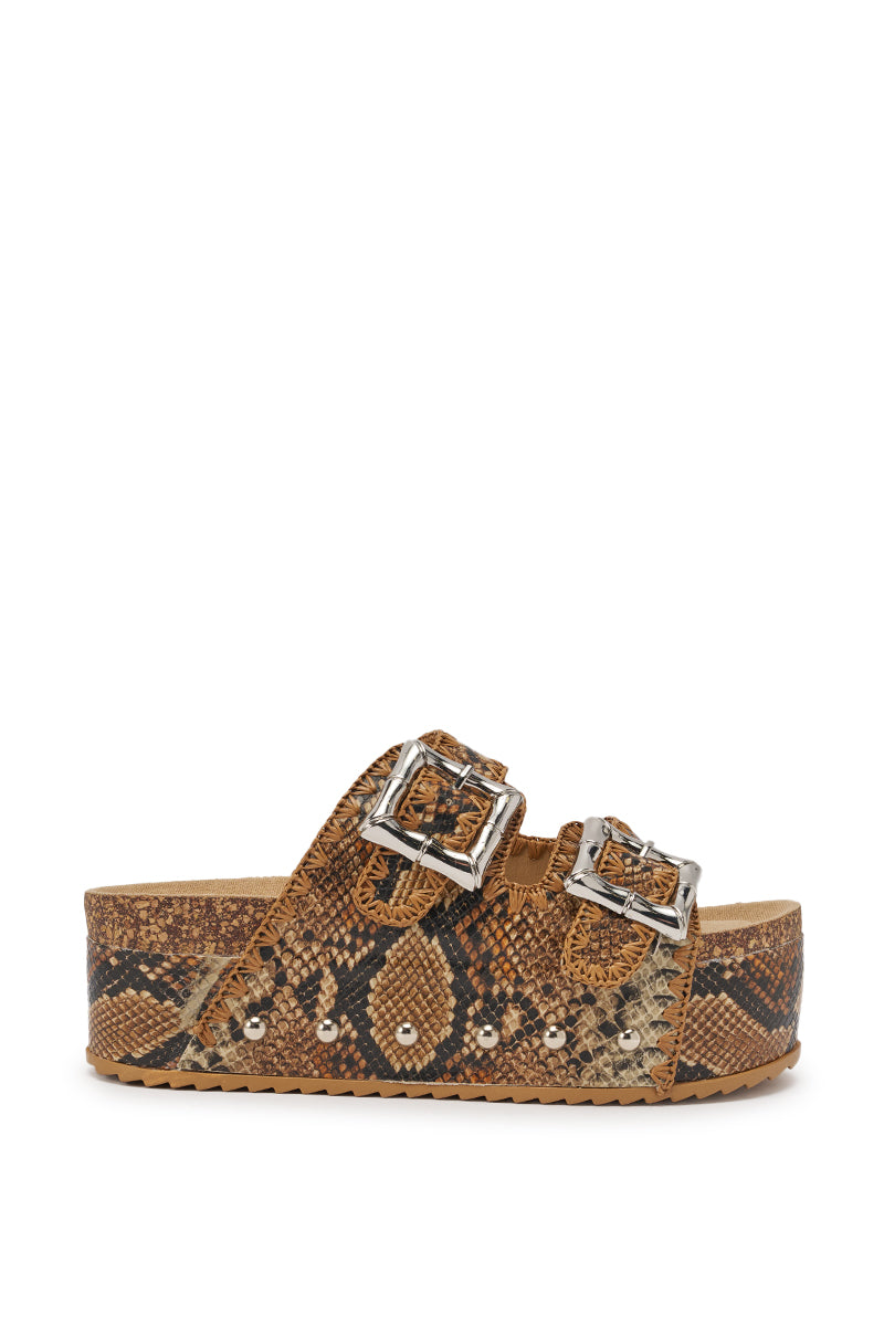 The AZALEA WANG OHKAY SNAKE FLATFORM STUD EMBELLISHED SLIP ON SANDAL features a brown and black snakeskin print, two wide faux leather straps with large silver buckles, and silver studs along the chunky platform sole. 3