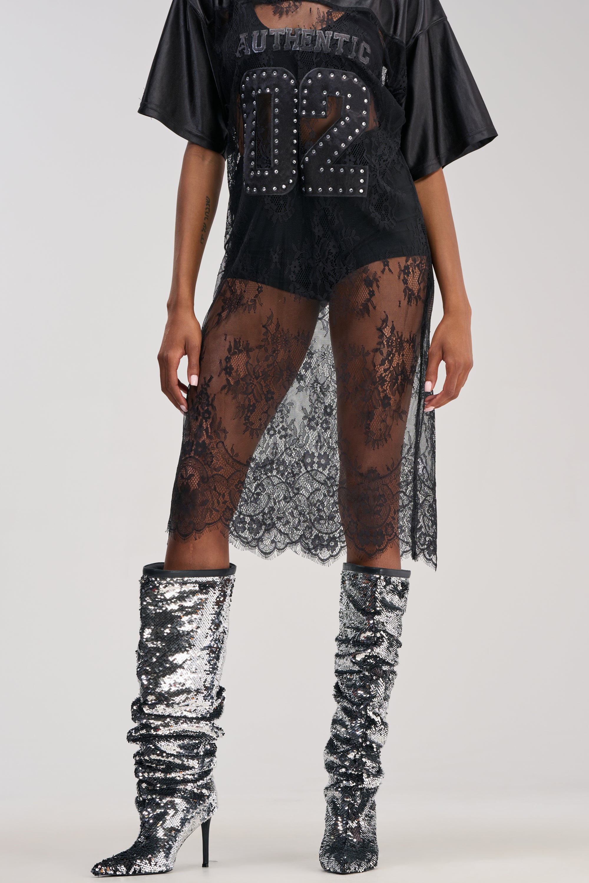 A person wearing a black oversized shirt, a sheer lace skirt, and the AZALEA WANG OLETHA SILVER SEQUIN STILETTO BOOT stands against a plain background, with only their lower body and part of the torso visible.