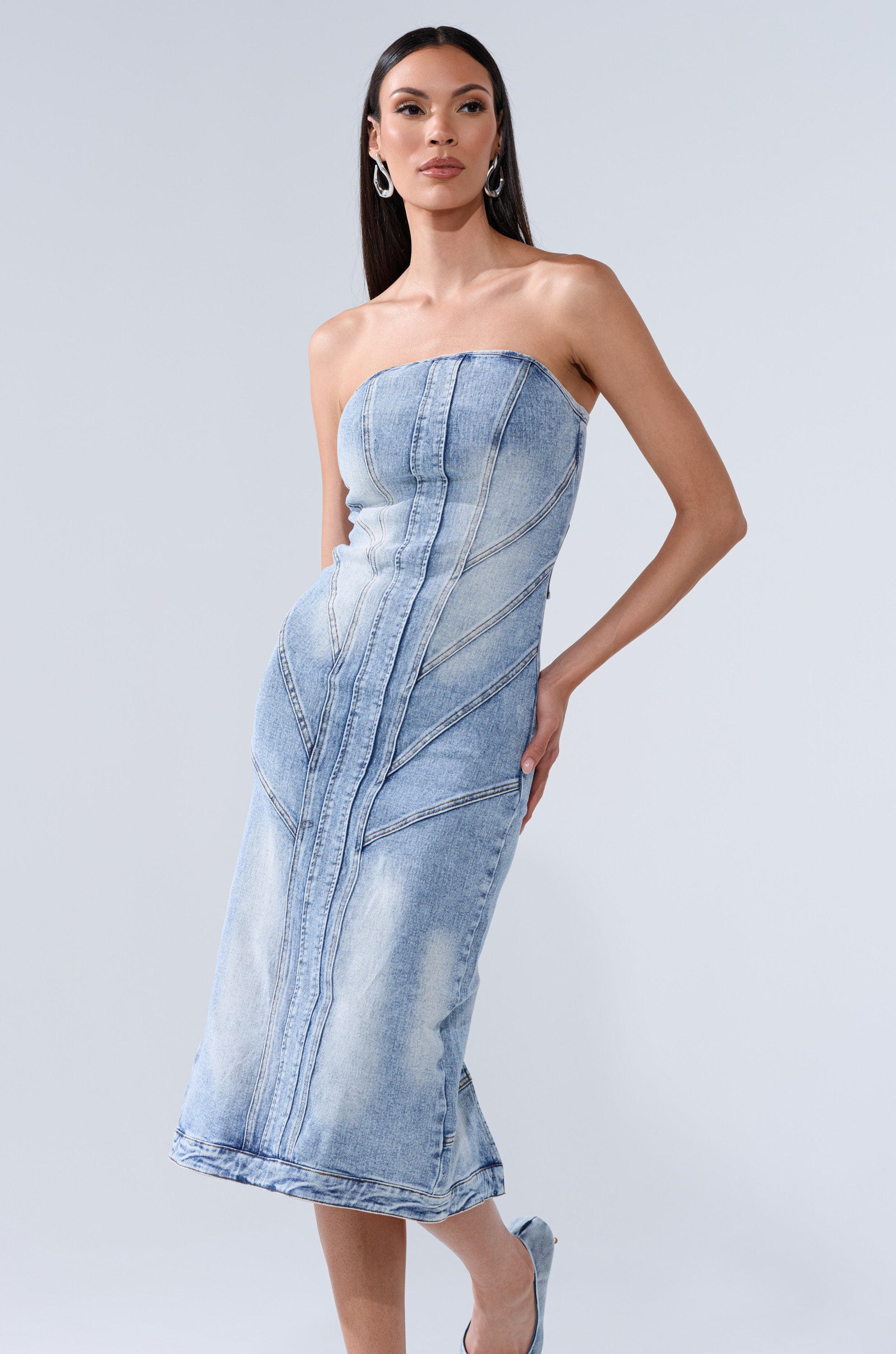 A woman models the BROOKLYN BADDIE DENIM MIDI DRESS, a strapless design featuring faded detailing and prominent seam lines, against a plain light background.