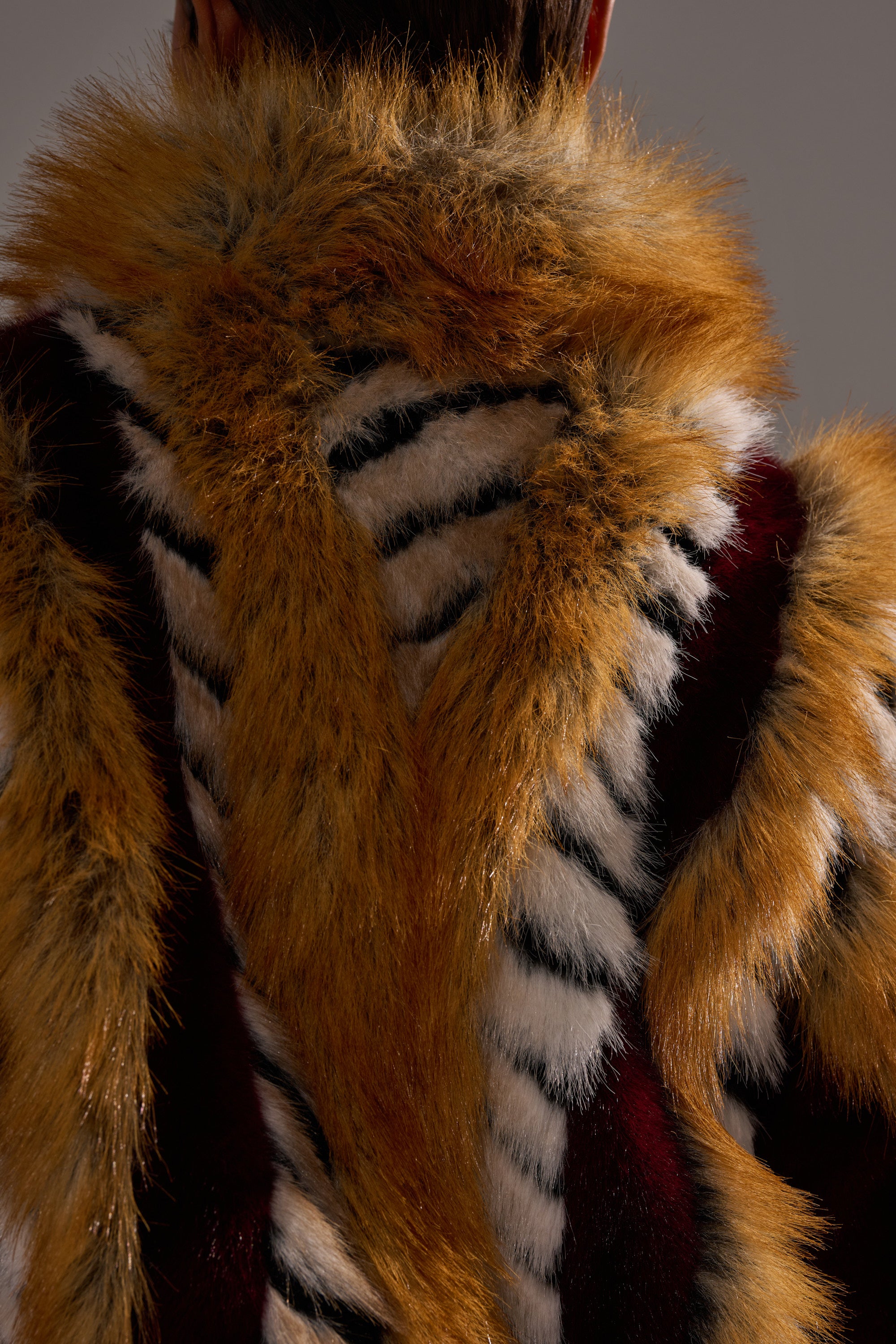Close-up of a person's back in the OLYMPIA PANELED FAUX FUR coat, featuring oversized panels in brown, black, white, and reddish stripes for a bold, animal-inspired look.
