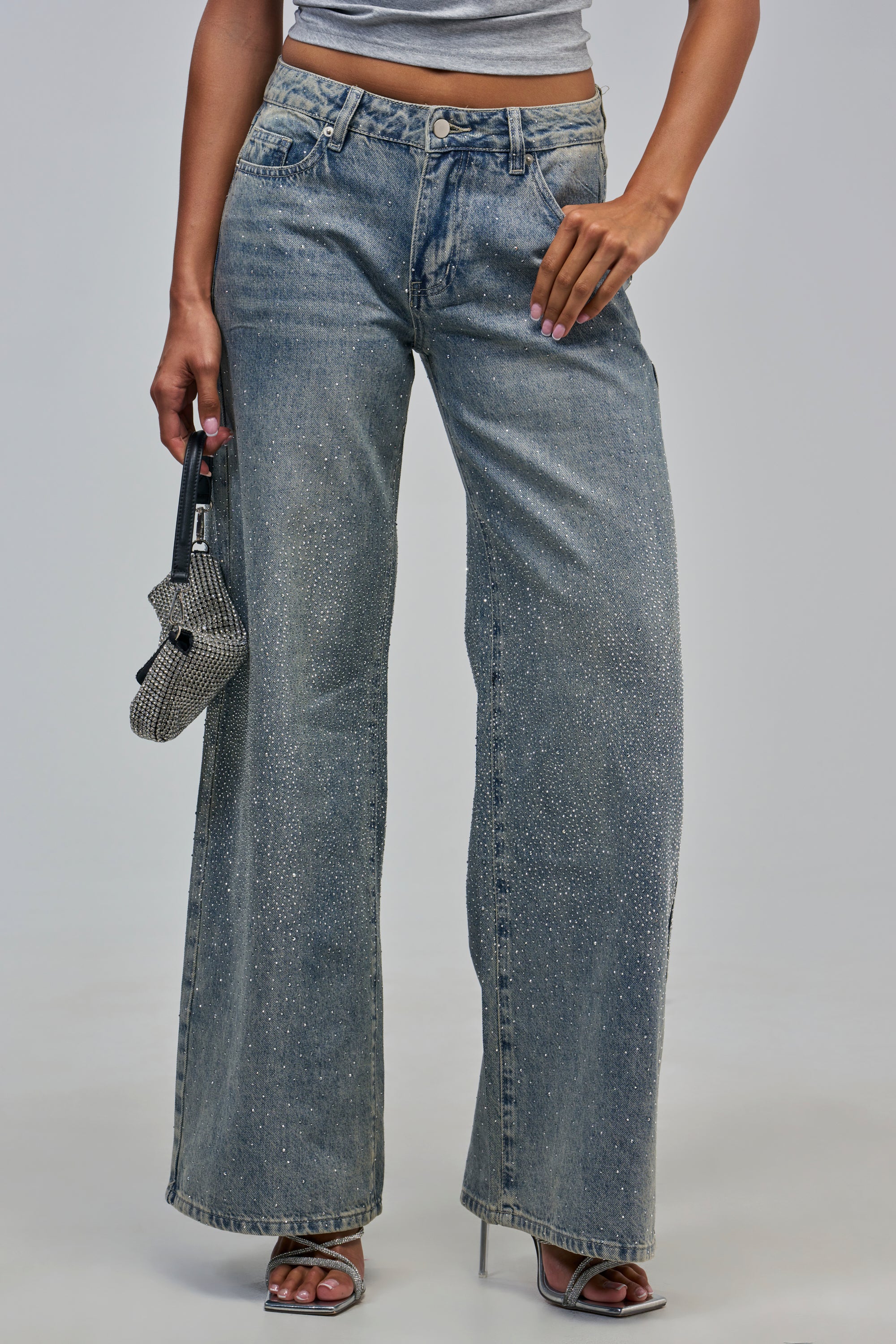 SLOANE LOW RISE ULTRA BAGGY DENIM in a light wash with rhinestone detailing, worn with silver strappy heels and a small, sparkly handbag.