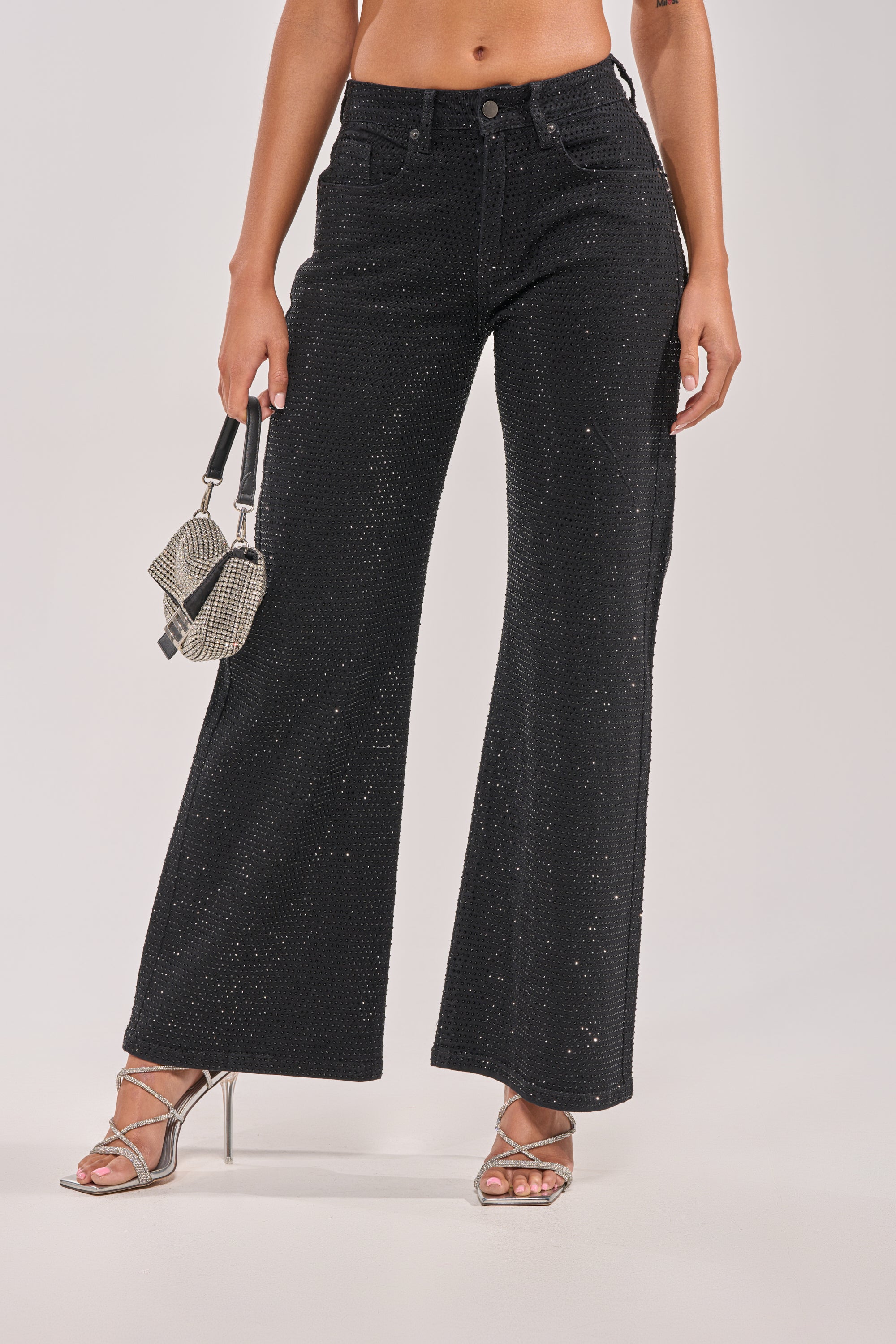 A person wearing SHINING BRIGHT RHINESTONE DENIM featuring a subtle sparkling pattern, paired with silver strappy heels and a small silver handbag. 0