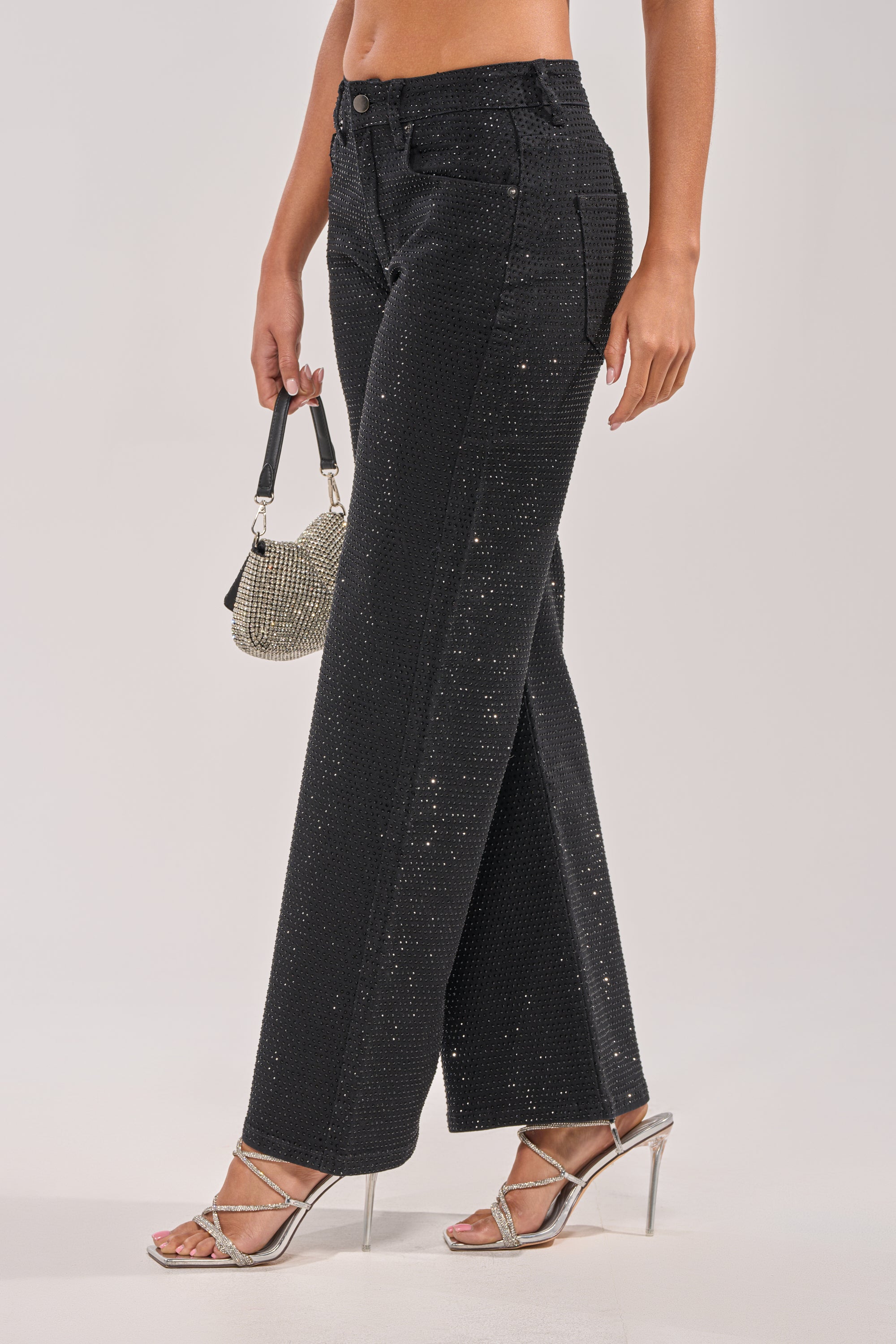 A person models the SHINING BRIGHT RHINESTONE DENIM with silver high-heeled sandals, holding a small glittery handbag against a plain background. The photo is cropped from the shoulder down. 2
