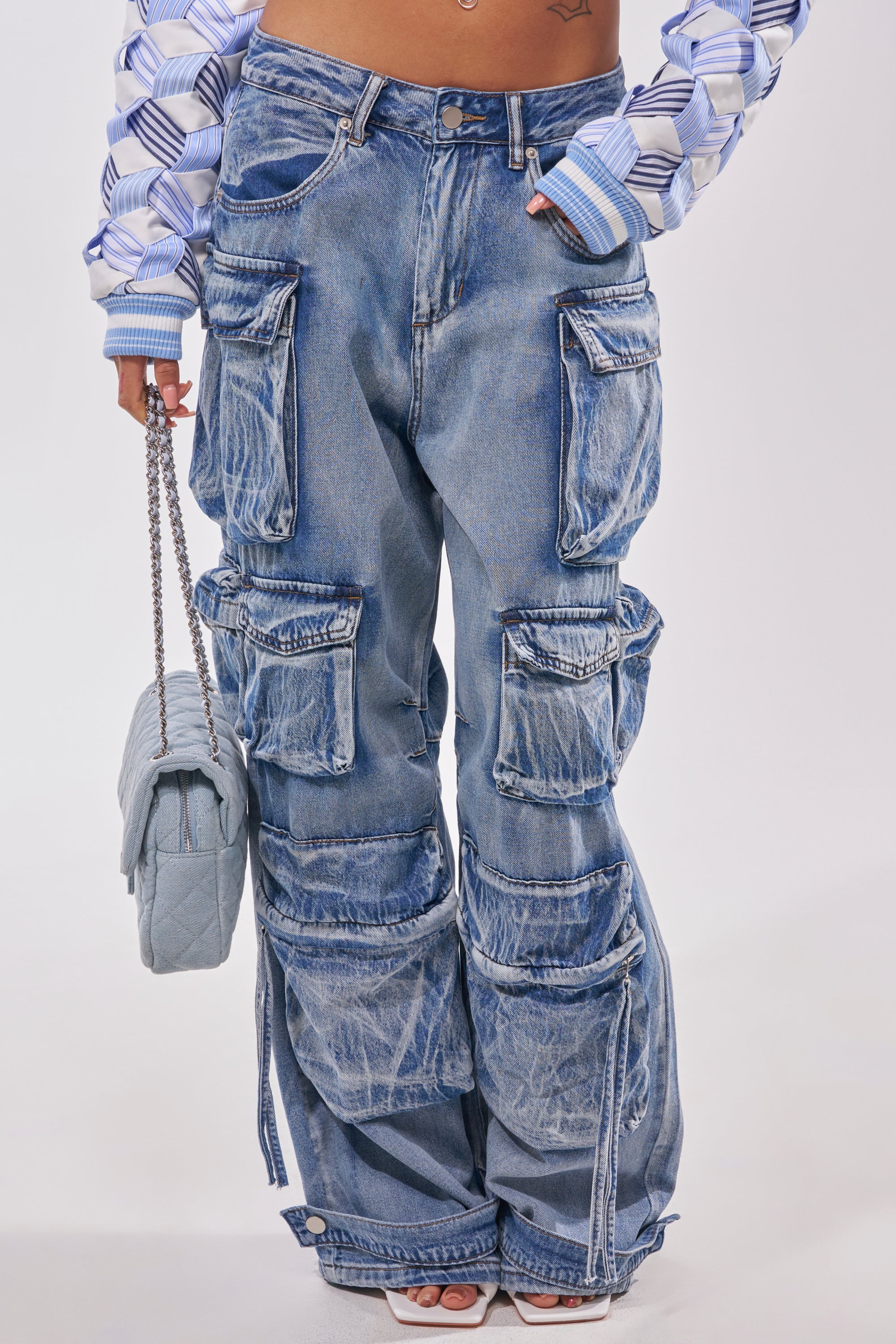 A person flaunts streetstyle in EASY ENOUGH CARGO DENIM—loose, light blue cargo pants with large pockets—paired with a patterned cropped jacket, a quilted blue handbag, and open-toe heels. 1