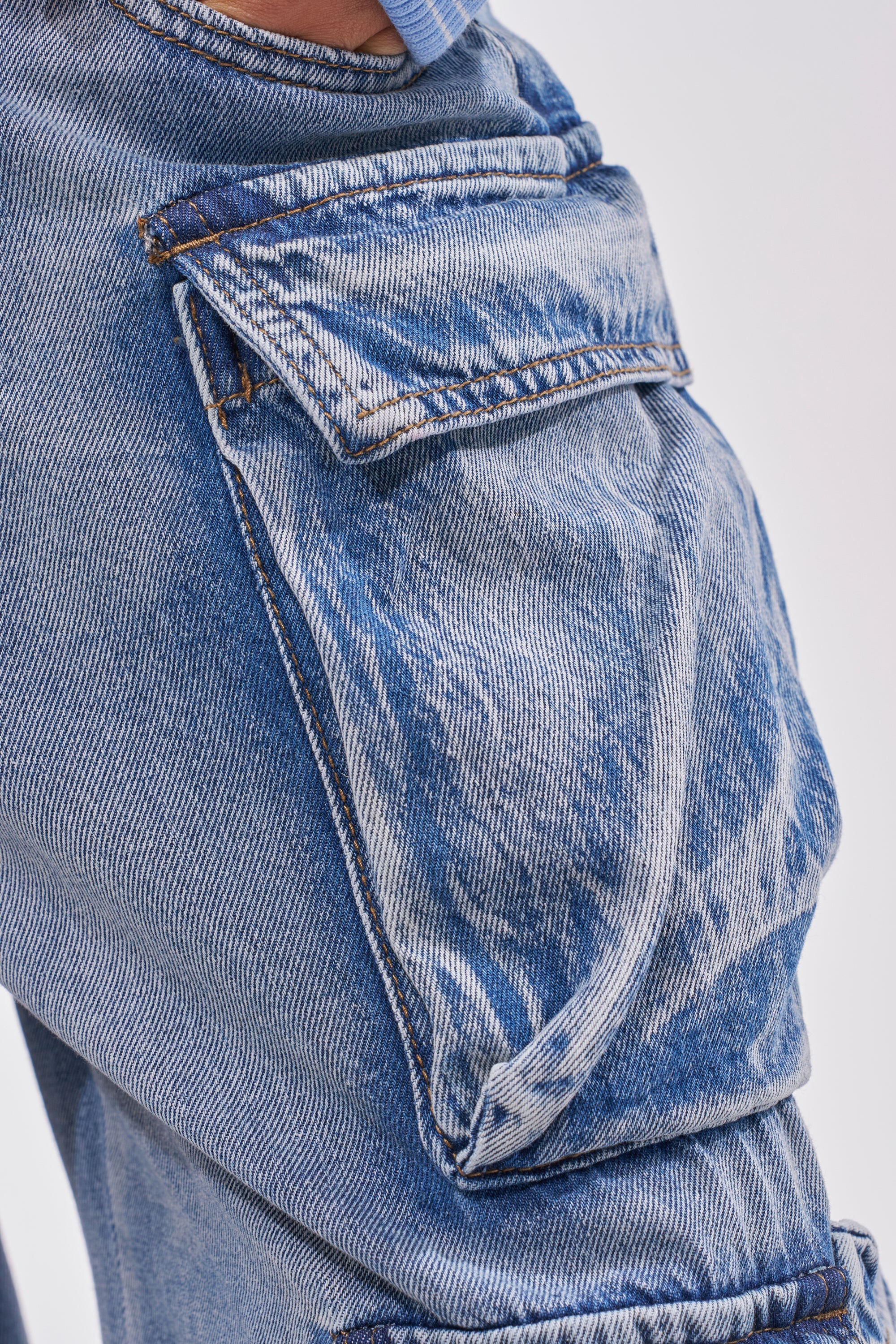 Close-up of the EASY ENOUGH CARGO DENIM, featuring a light blue wide-leg design with detailed stitching, flap pocket closure, and a faded streetstyle wash on textured denim. 5