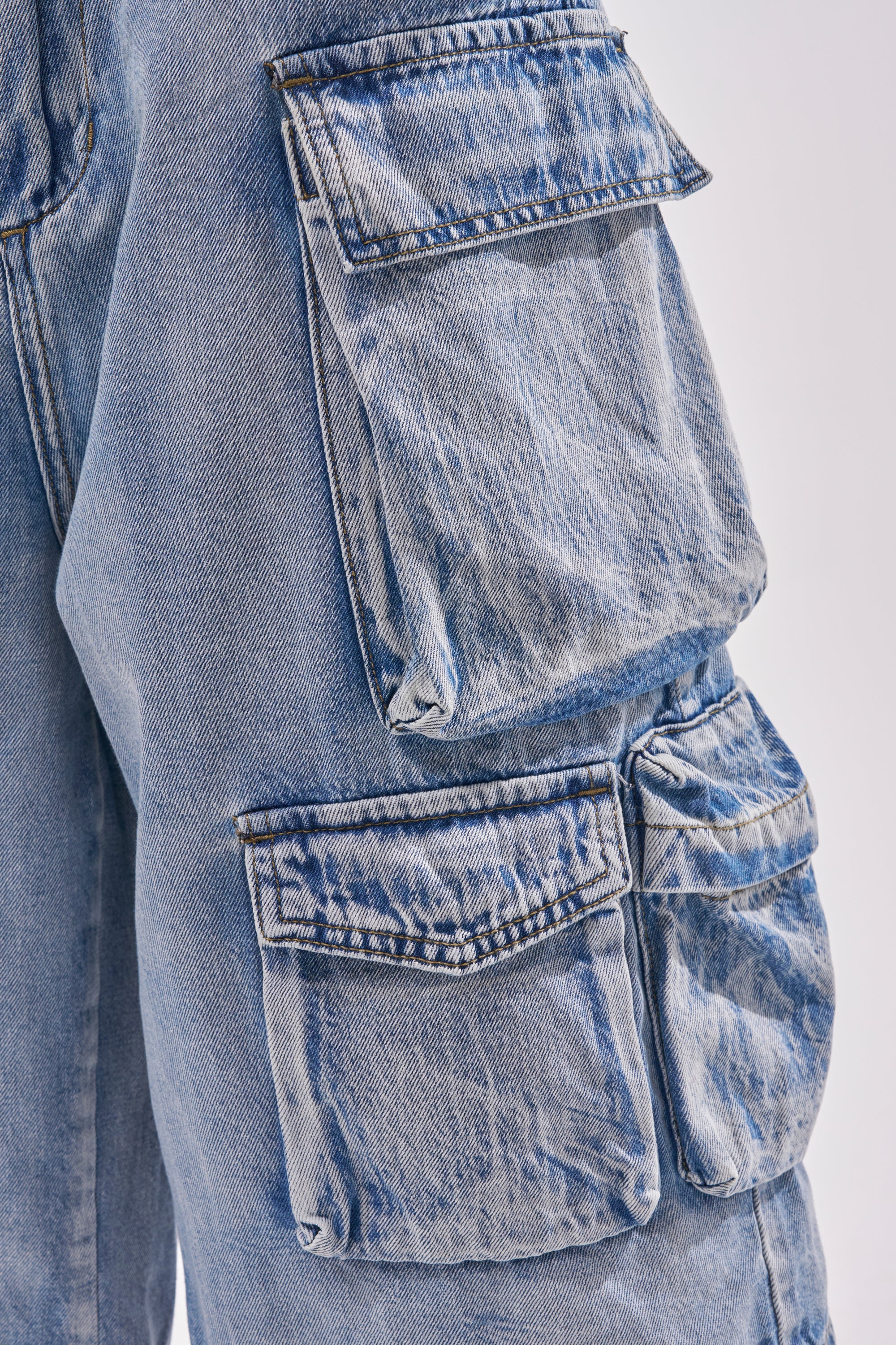 Close-up of the TOO MUCH FUN CARGO BERMUDA SHORT in light blue denim, featuring two large flap pockets with visible stitching and a slightly worn, textured look—ideal for a laid-back streetwear vibe. 6