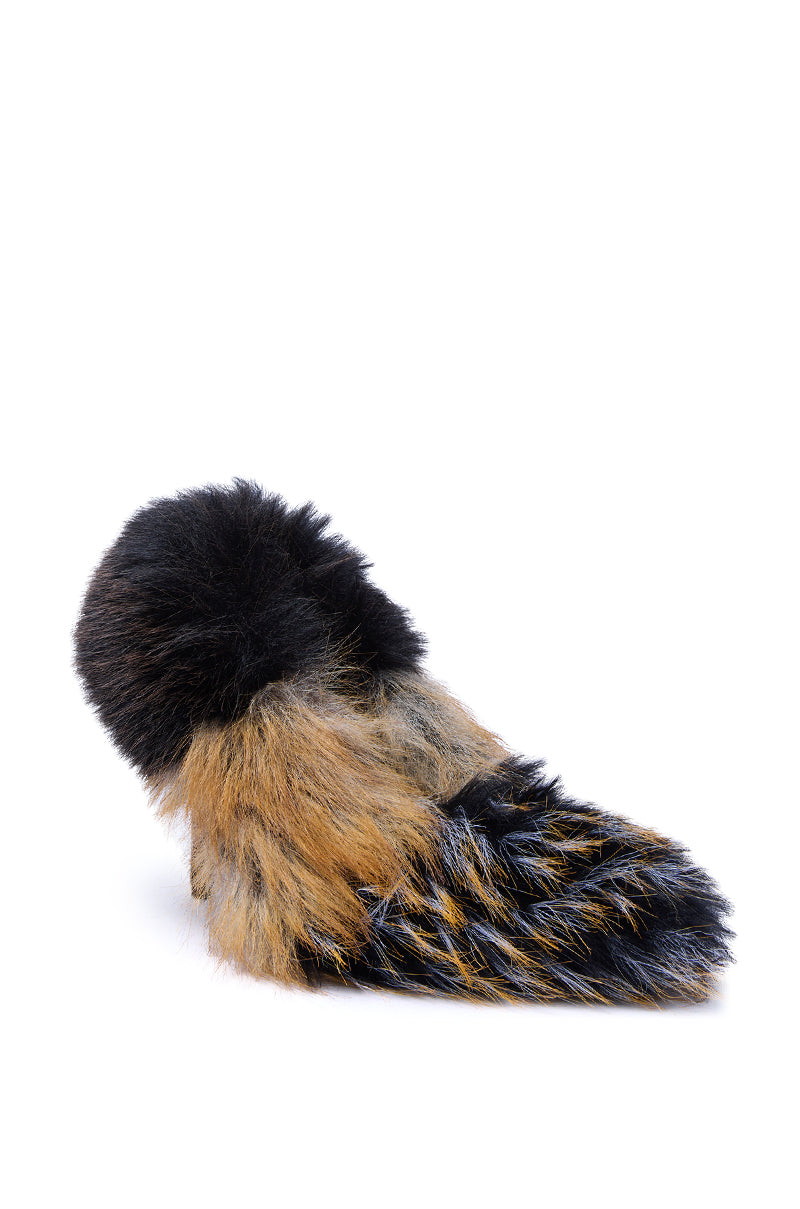 The AZALEA WANG OMIRCON Black and Tan Fur Stiletto Pump sits beside a fluffy, multicolored faux fur tail in hues of brown, black, and dark gray, all displayed on a white background.