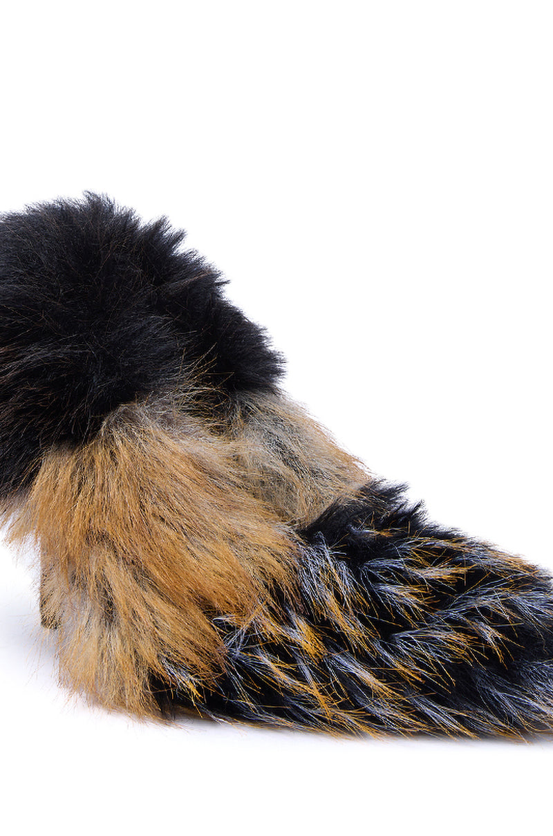 A fluffy, multicolored animal tail with black, brown, and gray fur rests on a white background—its hues echo the AZALEA WANG OMIRCON BLACK AND TAN FUR STILETTO PUMP.