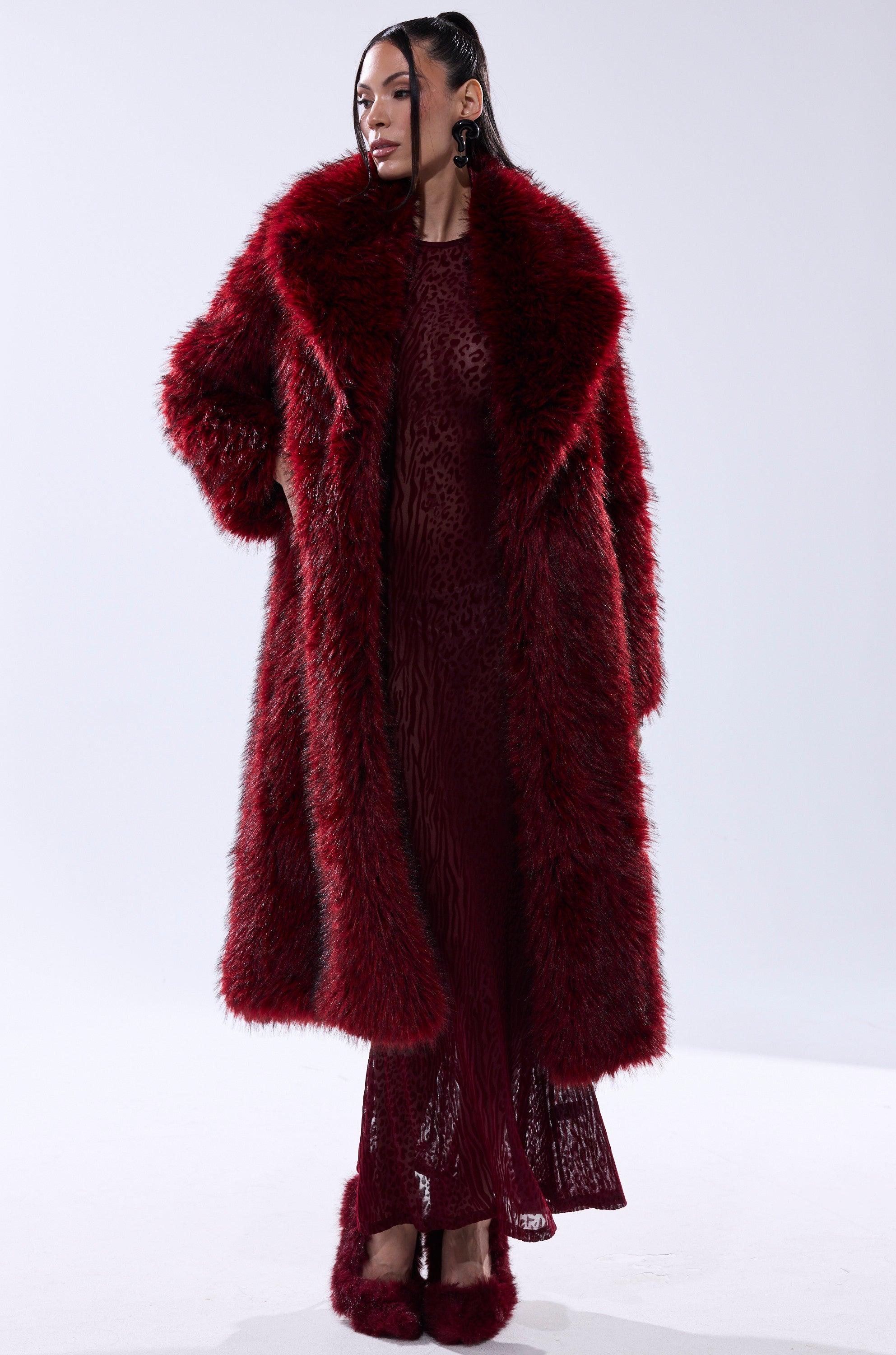 A woman wears the OSLO FAUX FUR COAT IN RED MULTI over a matching dress and red furry slippers, posed against a plain white background.