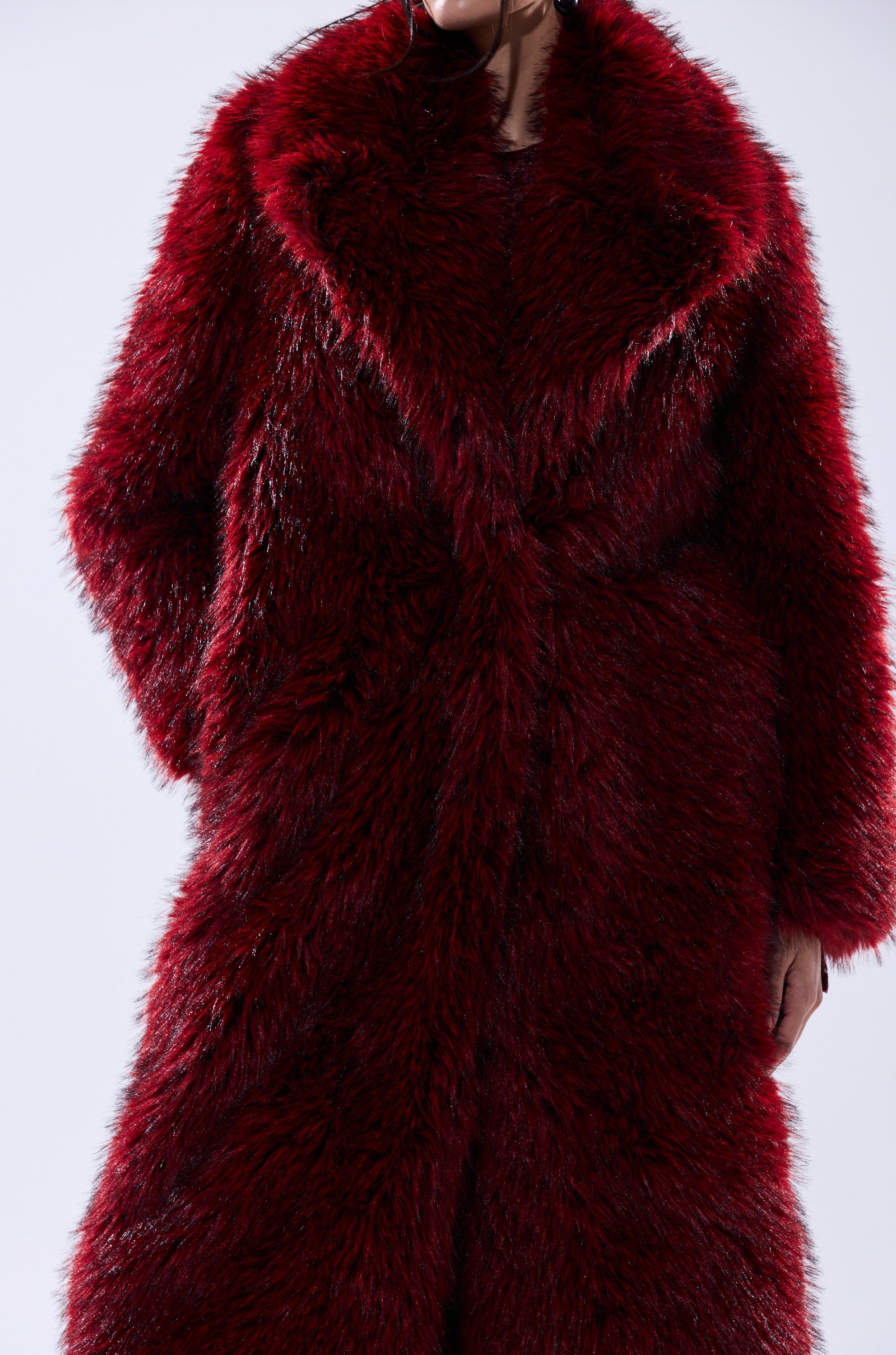 Model shown from the neck down wearing the OSLO FAUX FUR COAT IN RED MULTI, featuring a luxurious long deep red faux fur, oversized notched lapel, and large collar against a plain light background.