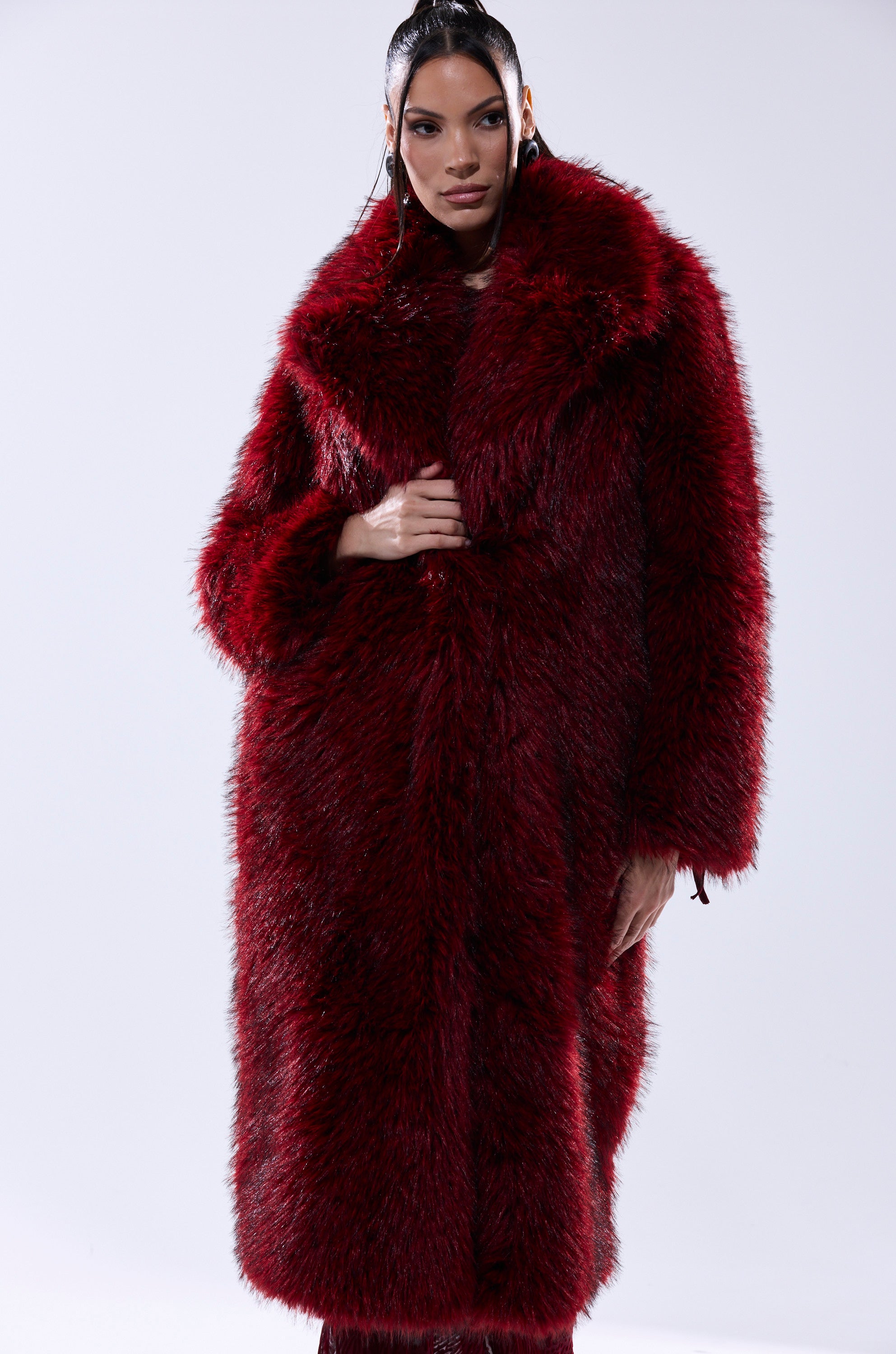A woman poses against a plain light background wearing the OSLO FAUX FUR COAT IN RED MULTI, featuring an oversized fit and wide collar.