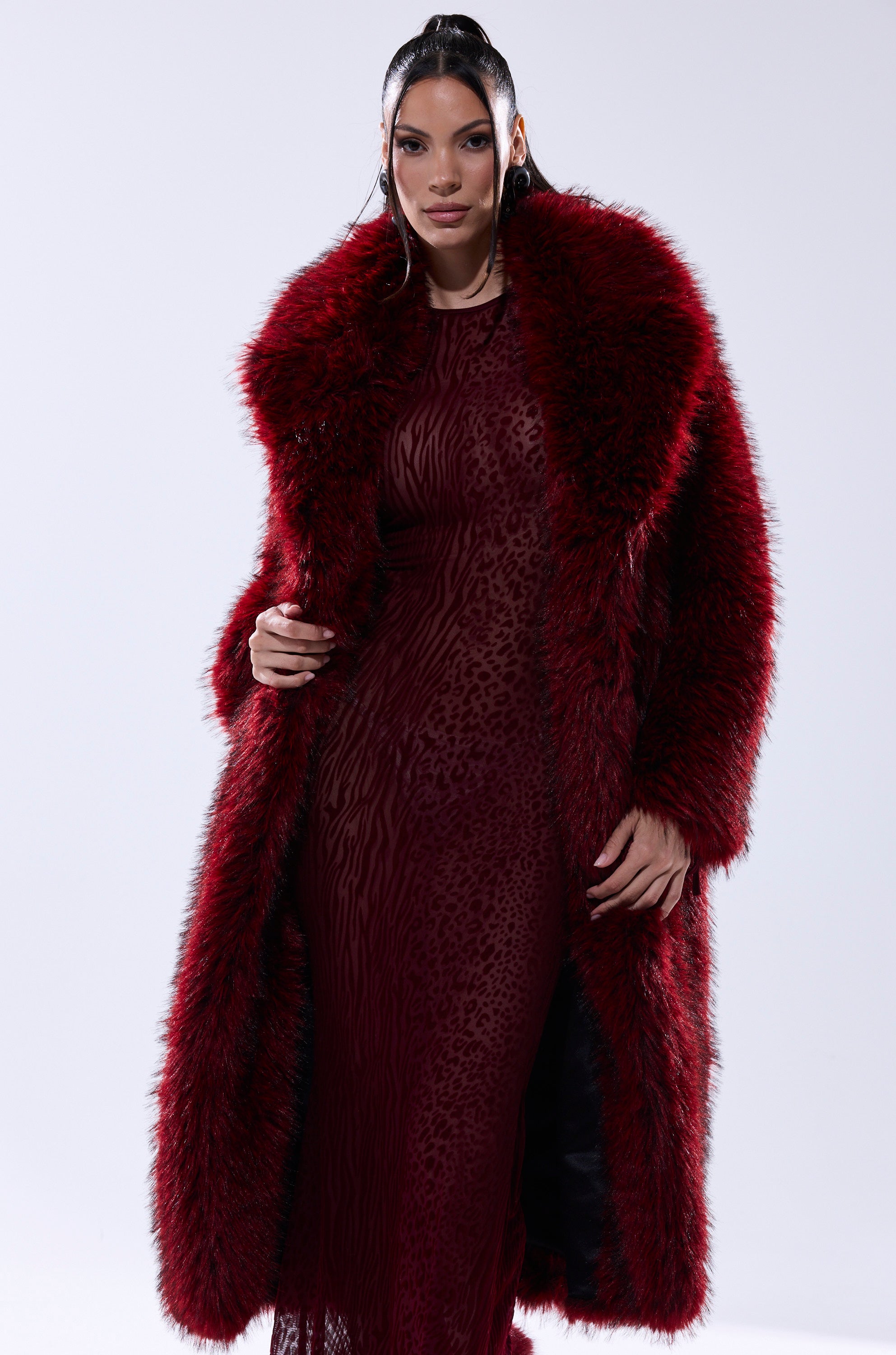 A woman poses confidently in the OSLO FAUX FUR COAT IN RED MULTI over a matching red dress, standing against a plain light background.