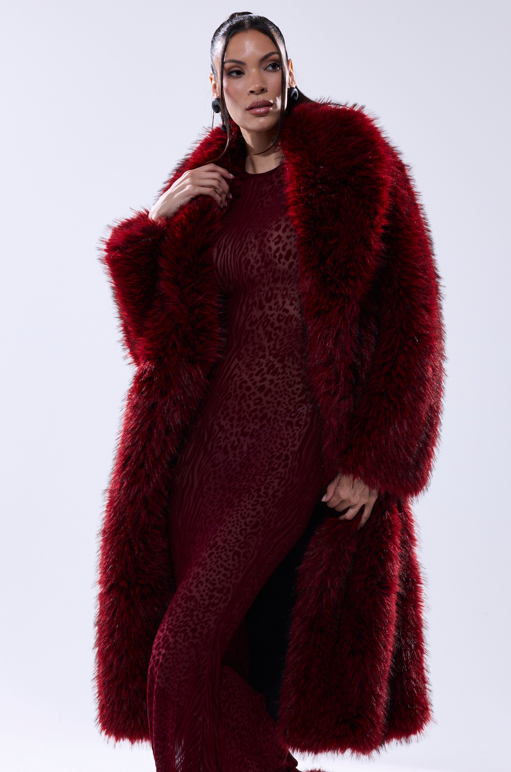 A woman poses confidently in the OSLO FAUX FUR COAT IN RED MULTI, layered over a sheer, form-fitting red leopard-print dress, set against a plain light background.