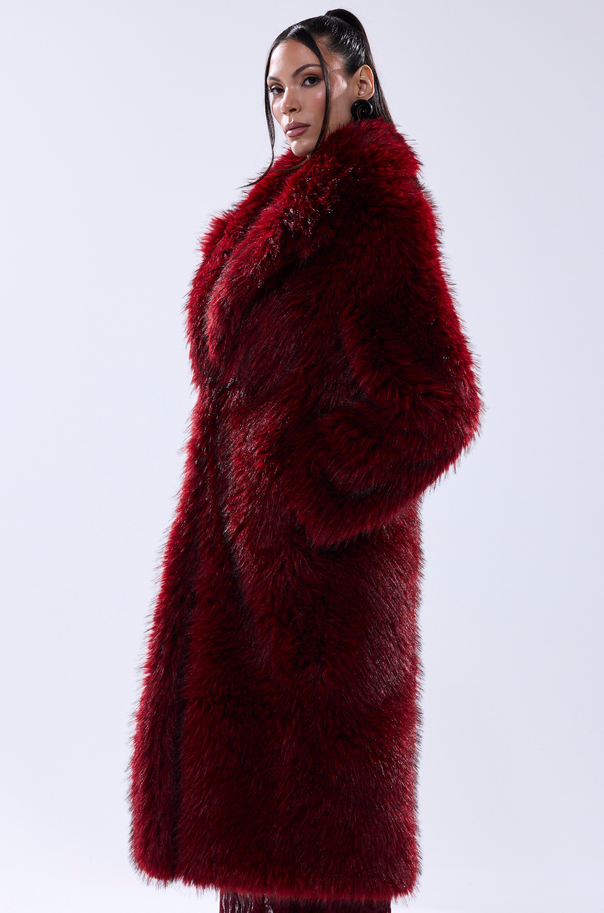 A woman stands against a plain light background, hands in pockets, confidently wearing the OSLO FAUX FUR COAT IN RED MULTI.