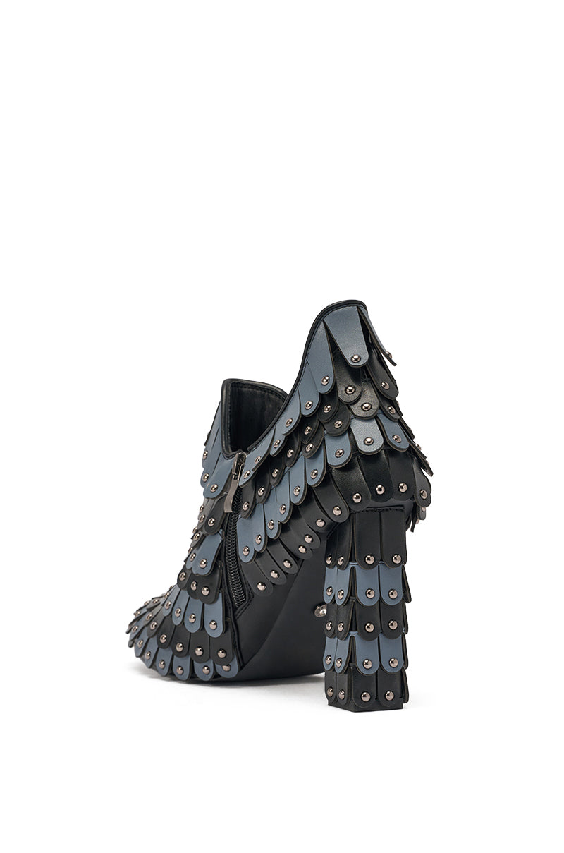 The AKIRA GOLD OSTENTATION BLACK ABSTRACT PUMP features a block heel and overlapping black faux leather scales with a studded design, resembling armor or dragon scales, shown from the back against a white background. 5