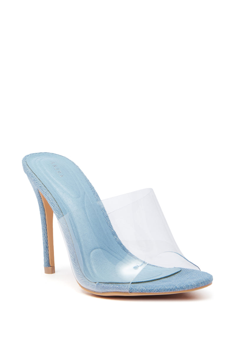 The AKIRA OSWEGO DENIM NEW SLIP ON MULE SANDAL features light blue denim with a transparent strap, a textured fabric heel and sole, and an open-toe design. Its comfort cushion insole ensures both style and comfort.