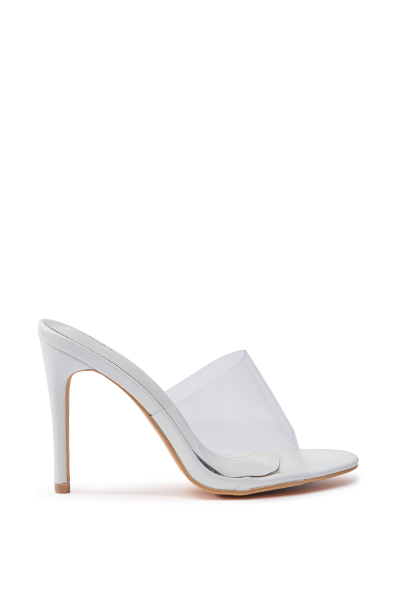 The AKIRA OSWEGO WHITE SLIP ON SANDAL is a high-heeled mule with a translucent PVC vamp, a white sole, and a slender stiletto heel, showcasing a minimalist design on a plain white background.