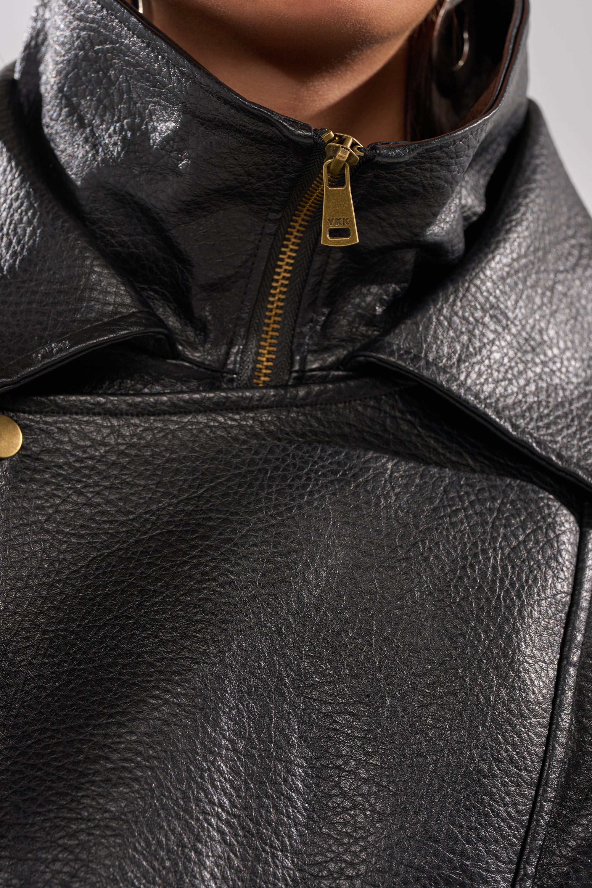 Close-up of a person wearing the ERIKKA OVERSIZED MOTO, showcasing its biker-inspired collar, textured black faux leather, gold zipper, and snap button details at the collar and upper chest.