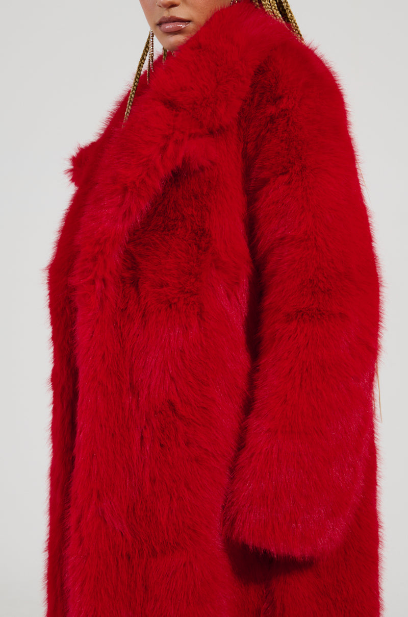Someone is wearing the OXFORD FAUX FUR TRENCH in a vibrant red, featuring an oversized maxi-length silhouette, as they stand against a plain background. The emphasis is on the coat's texture and color, with the person's face partially out of frame.
