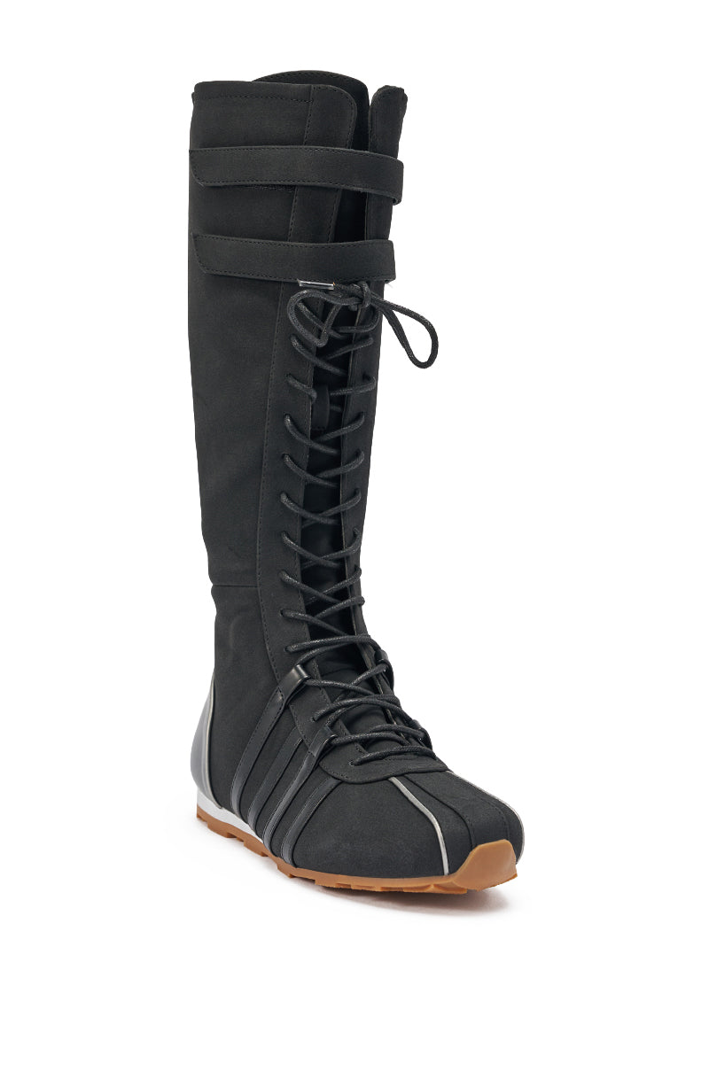 The AZALEA WANG OZZY BLACK FLAT SNEAKER is a single black knee-high boot with a flat light brown sole, lace-up front, decorative shaft straps, and minimalist sporty-chic design. 4