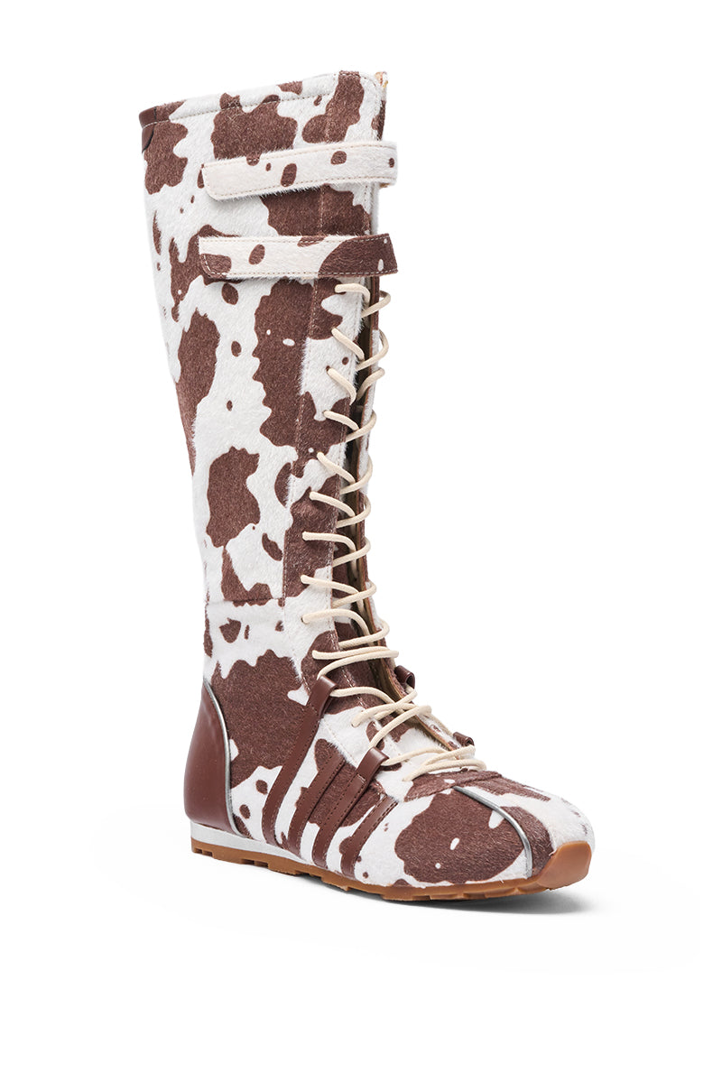 The AZALEA WANG OZZY BROWN MULTI FLAT KNEE HIGH SNEAKER features faux pony hair in a brown and white cow print, a lace-up front, Velcro strap at the top, and a brown sole and toe for a playful, standout look. 4