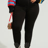 A person wearing high-waisted black pants paired with a colorful striped sweater, holding a small leopard print handbag, and sporting black lace-up combat boots. Their outfit would look equally stylish with dark wash denim or the REBECCA ULTRA HIGH RISE SKINNY PLUS jeans.