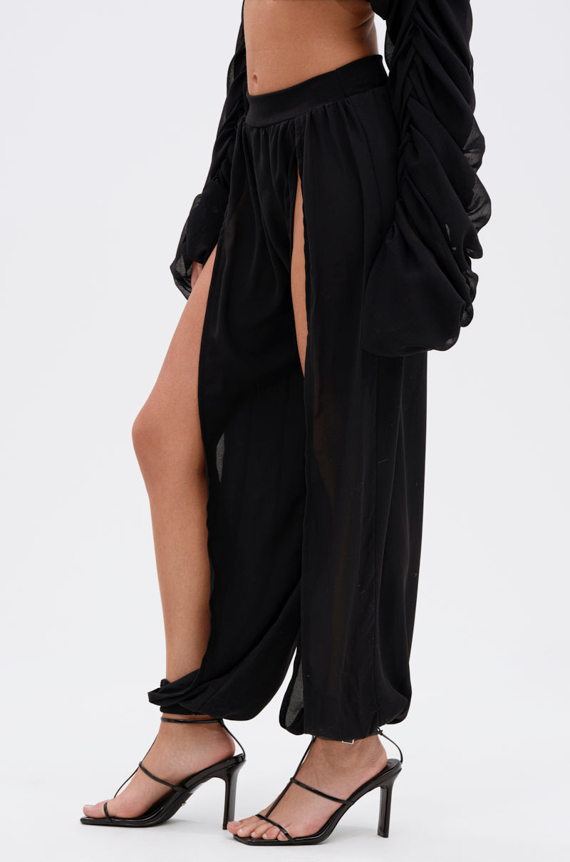 Someone stands against a plain white background wearing the COOL WITH ME JOGGER WITH FRONT SLITS in black, paired with a matching long-sleeve top and black heeled sandals. 4
