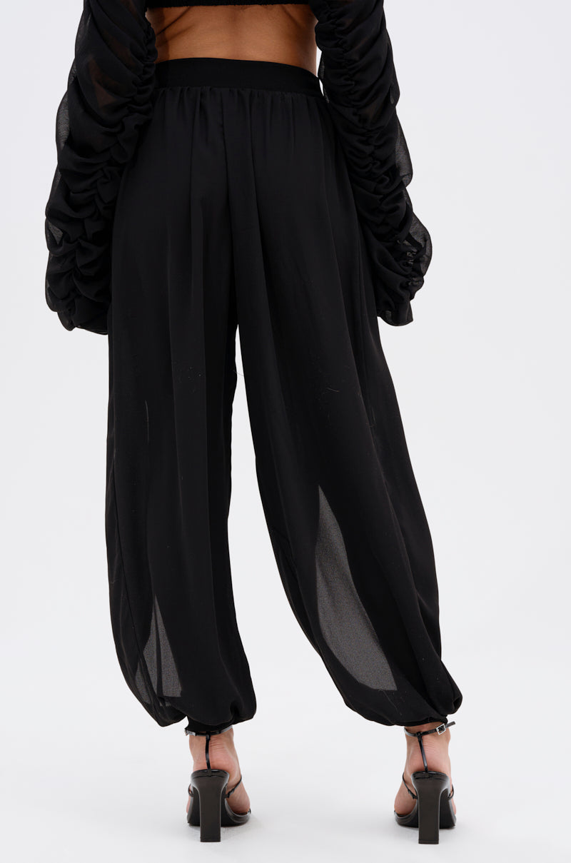 A person is shown from the back wearing COOL WITH ME JOGGER WITH FRONT SLITS—black, high-rise, loose-fit joggers with ankle gathering—styled with a matching black top and high-heeled sandals against a plain white background. 5