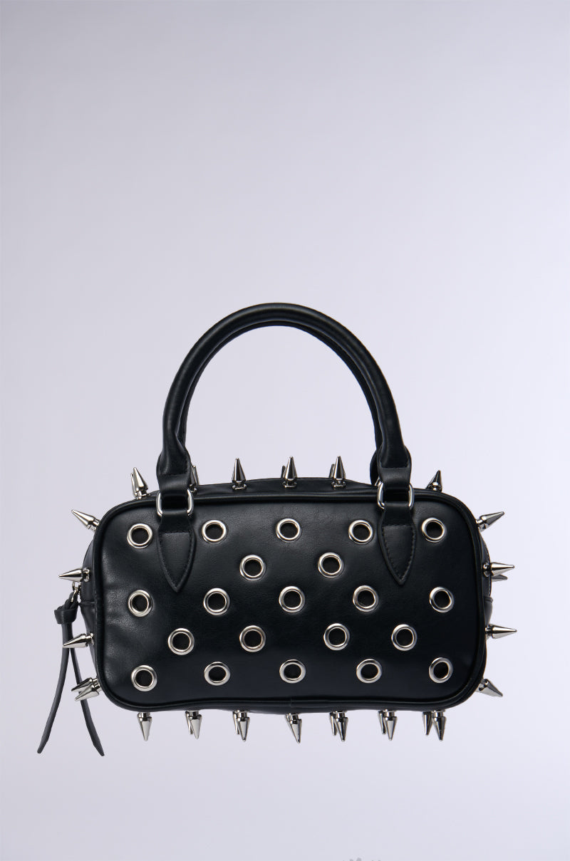 Introducing the SPIKED OUT EMBELLISHED PURSE: a stylish black purse adorned with silver spikes and circular grommets. This minimalist design features a convenient handle and is crafted from faux leather, making it an ideal accessory for a punk-inspired look. The bag is beautifully showcased against a plain gray background.