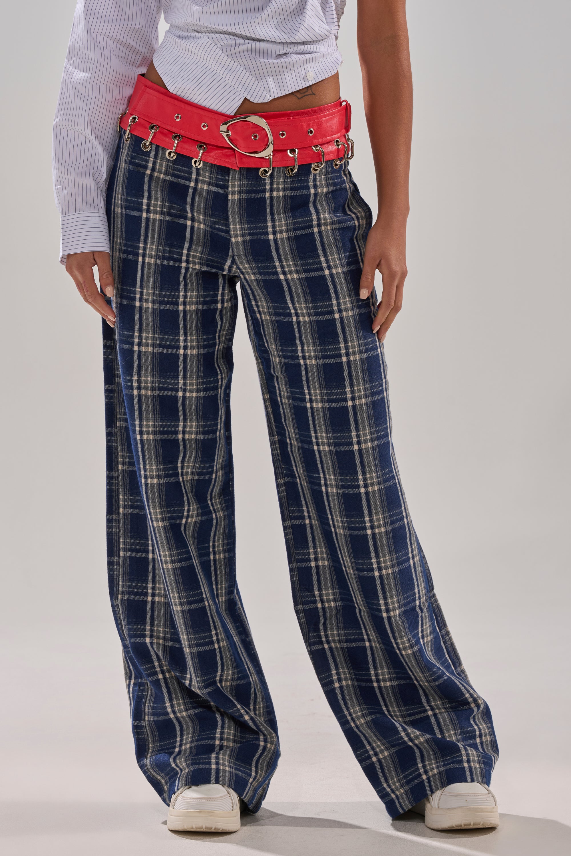 A person stands against a plain background wearing FREE STYLE LIFE PLAID TROUSER in blue plaid, paired with a blue and white striped shirt, red belt with silver grommets, and white sneakers.