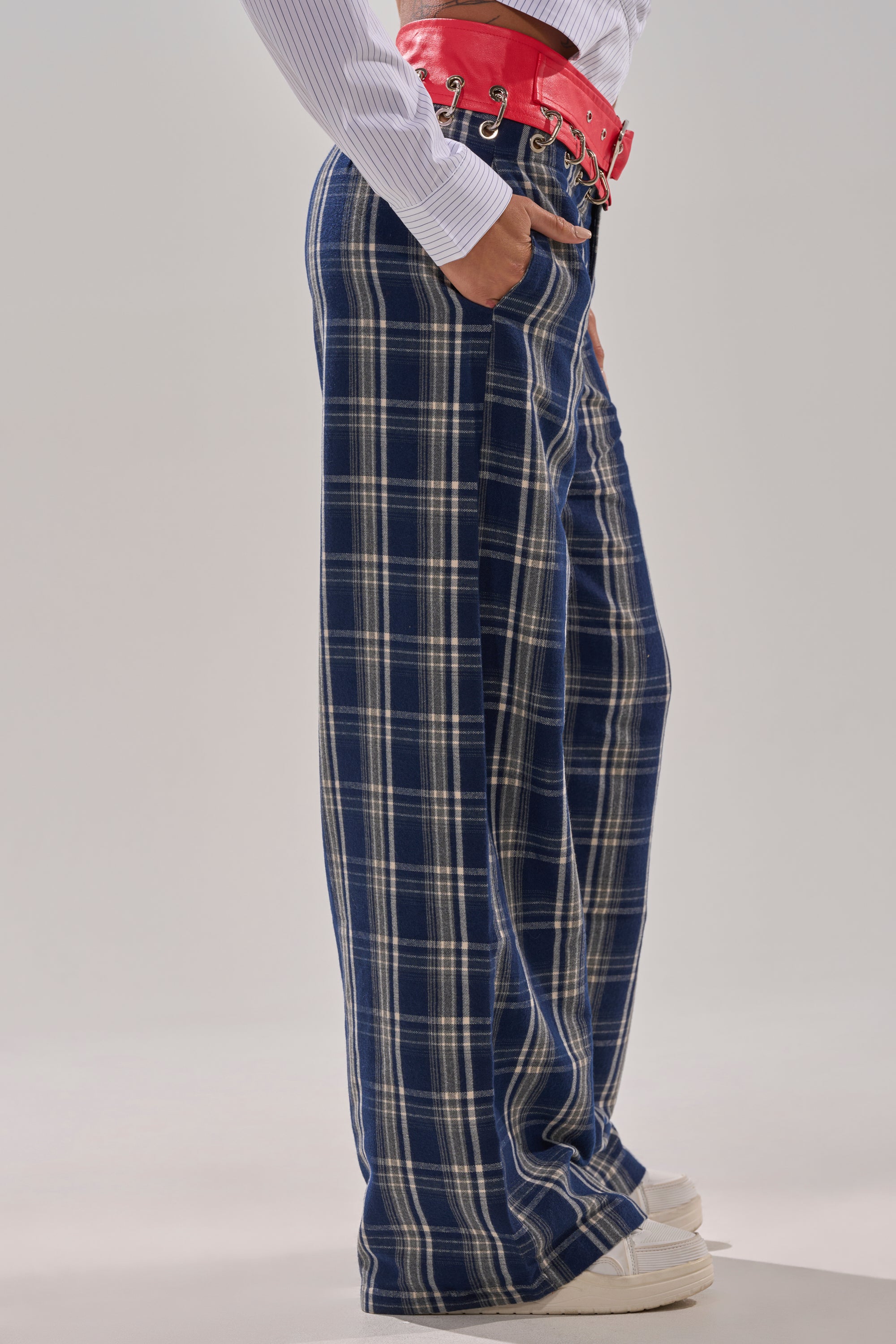 A person stands with hands in pockets against a plain background wearing FREE STYLE LIFE PLAID TROUSER, a white shirt, red corset-style belt, and white sneakers.