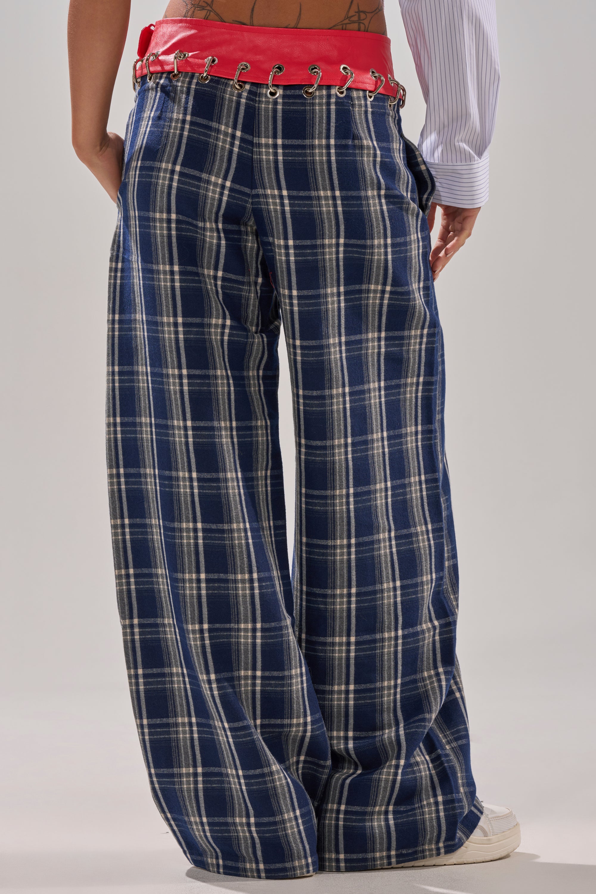 A person is seen from the back wearing the FREE STYLE LIFE PLAID TROUSER—loose-fitting, blue and white plaid with a red corset-style waistband and wide legs—paired with white shoes. A tattoo is visible on their lower back.