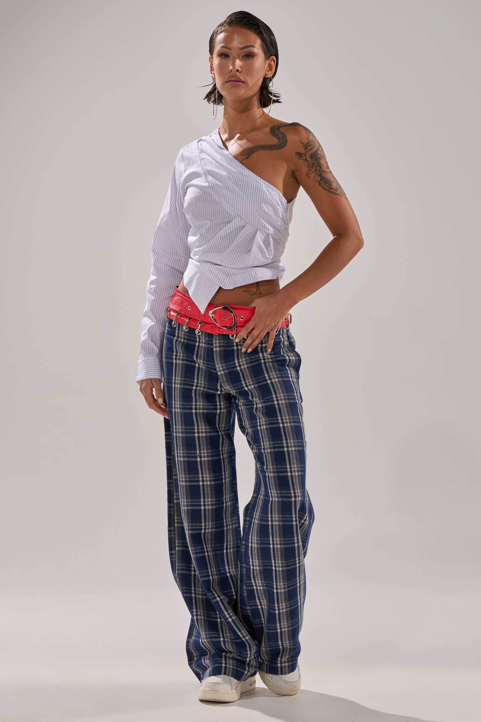 A person with short dark hair and an arm tattoo wears a one-sleeve white shirt, a bright red belt, white shoes, and the FREE STYLE LIFE PLAID TROUSER while standing confidently against a plain background.