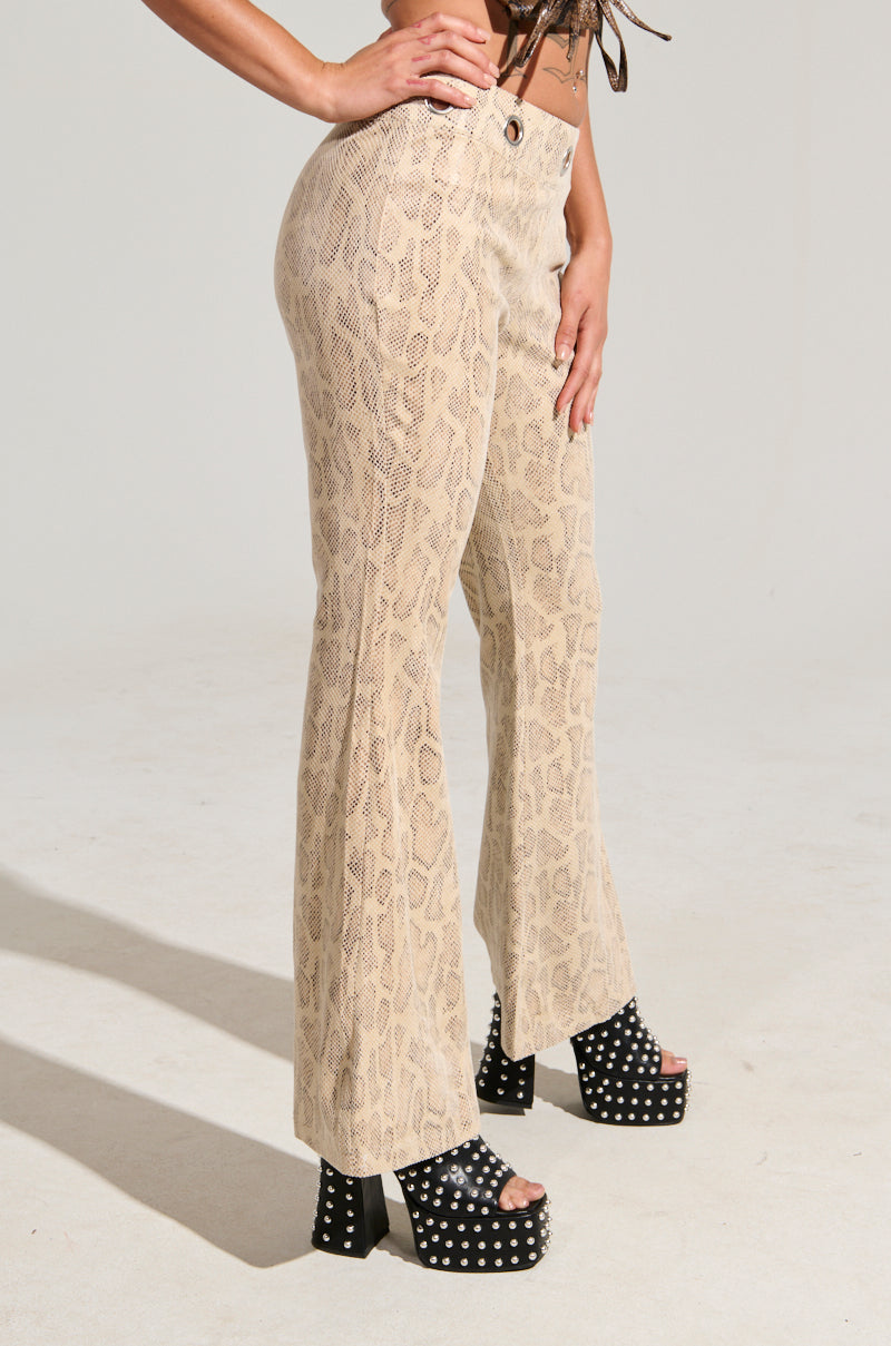 A person wearing the SNAKE CHARMER PANTS paired with black platform sandals adorned with silver studs stands against a plain backdrop. Their visible arms enhance the stylish and bold choice, showcasing the unique texture of faux suede.