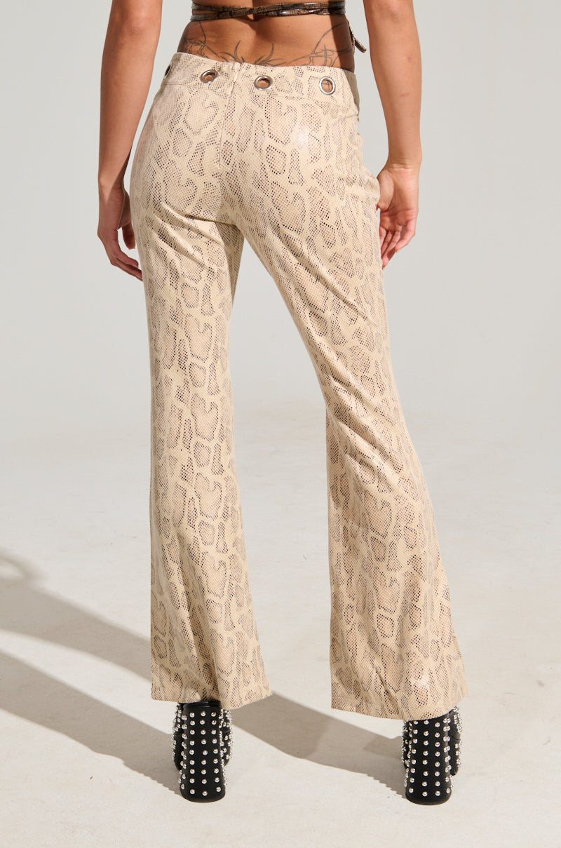 A person is wearing the SNAKE CHARMER PANT in tan paired with black studded heeled boots, facing away from the camera against a plain, light-colored background.