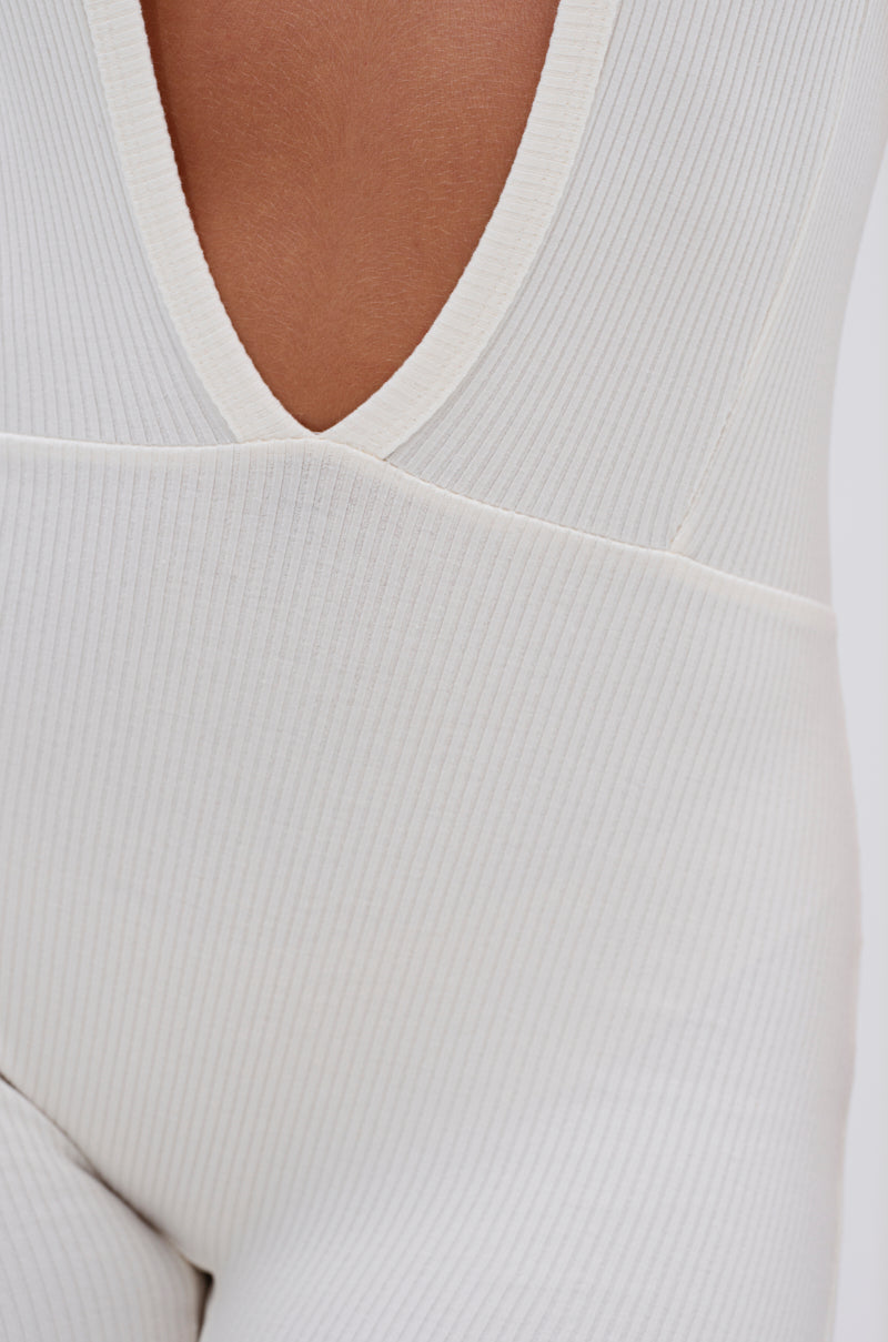 Close-up of a person wearing the MIXED MESSAGES PLUNGING JUMPSUIT—a white ribbed, sleeveless halter one-piece with a deep V-neckline. Visible fabric texture and seam details highlight its flattering fit and stylish design.