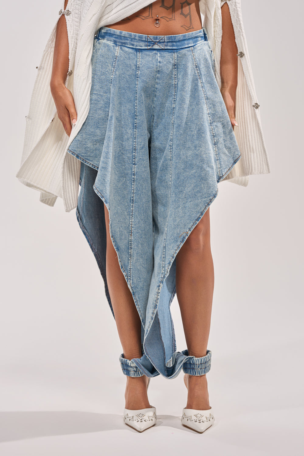 Wearing COOLEST EVER DENIM: asymmetrical, draped, high-rise denim bottoms with uneven hems and angular design for street-style edge—paired with a white textured cardigan and pointed-toe shoes. 3