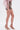 A person wears CLUB HIGH WAISTED PLEATHER SHORTS in taupe, a pink sheer blouse with loose sleeves, and tan strappy heeled sandals while standing against a plain white background.