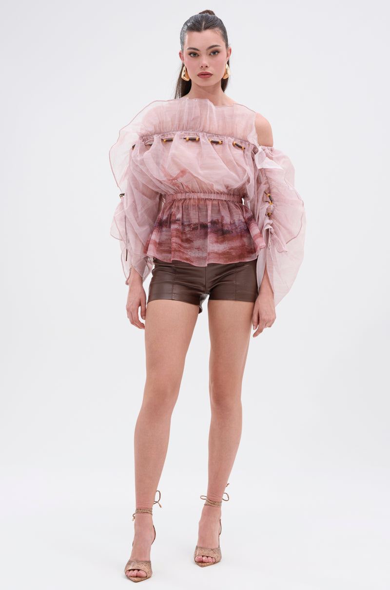 A woman faces forward wearing CLUB HIGH WAISTED PLEATHER SHORTS with a sheer, ruffled pink off-the-shoulder blouse, gathered sleeves, strappy heels, gold earrings, and her hair tied back. 4