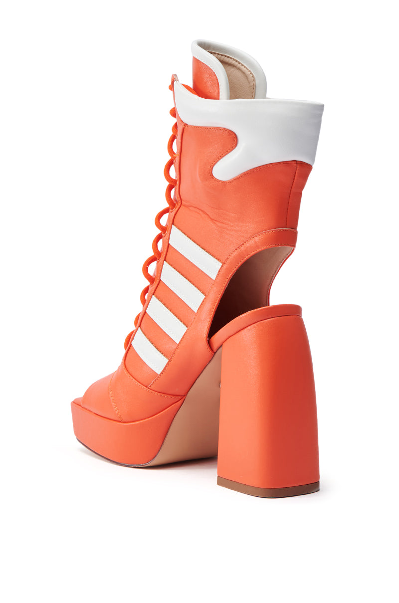 The AZALEA WANG PAMINA ORANGE CHUNKY SANDAL is a vibrant faux leather high-heeled boot with white stripes and an open heel. It features a chunky platform inspired by sandals with front laces, combining sporty elements with high-fashion style.