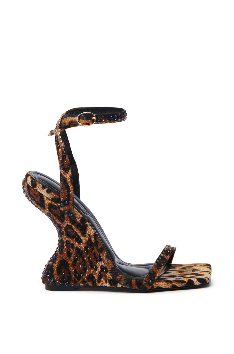 The AZALEA WANG PANTHERESS LEOPARD WEDGE SANDAL is a stunning suede textile sandal with a unique design, featuring an ankle strap with a buckle, small decorative studs along the edges, and rhinestone embellishments, elegantly showcasing an open toe and heel.